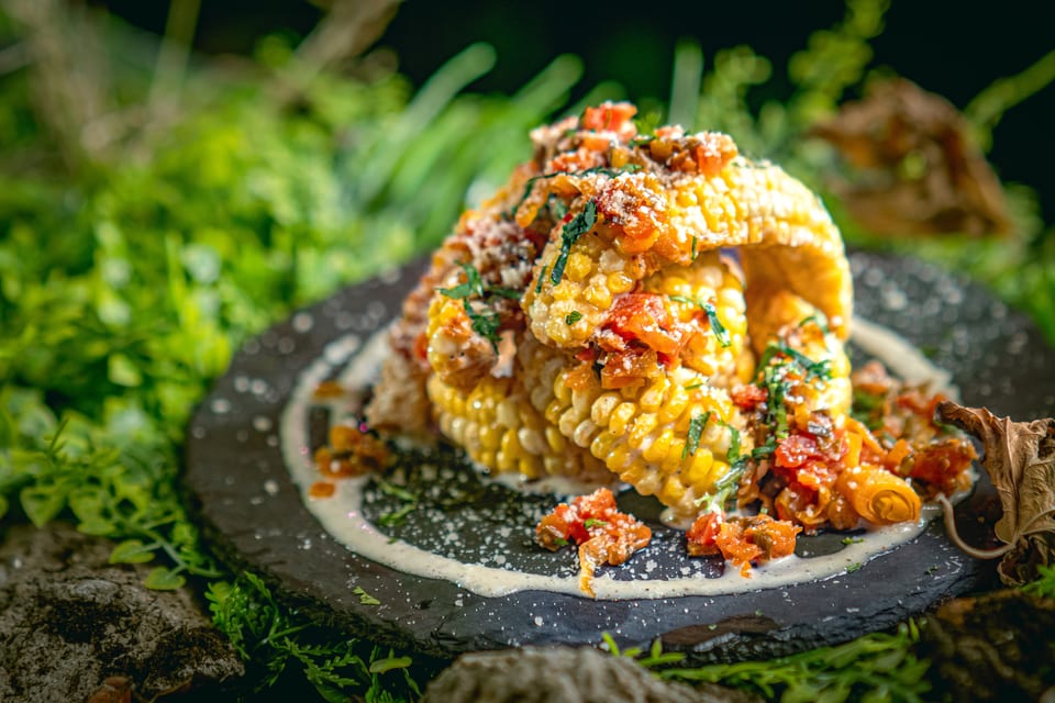 Grilled corn on the cob, topped with red peppers, herbs, and a creamy white sauce.