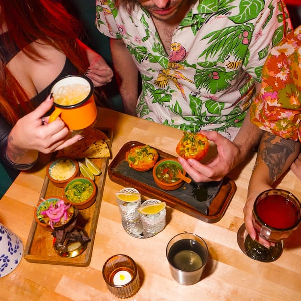 Three people enjoying drinks and small plates of Mexican food at a lively restaurant.
