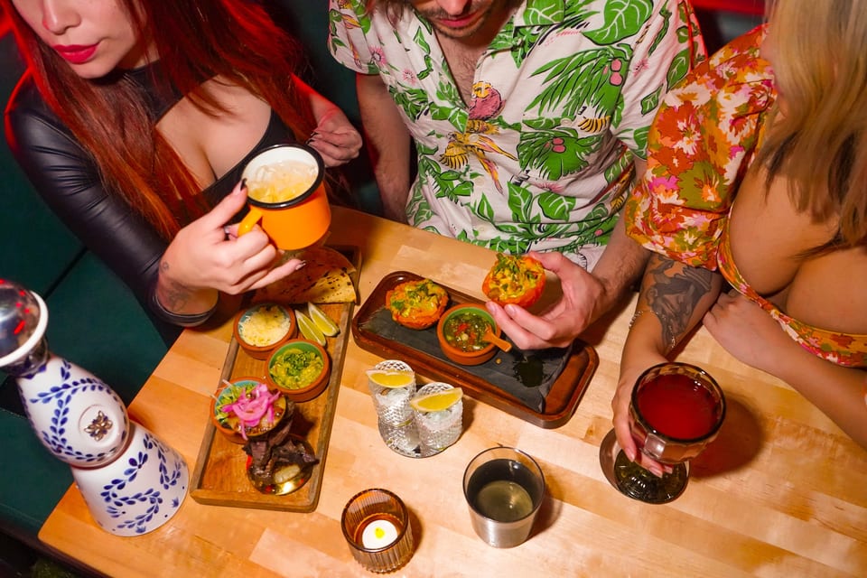 Three people enjoying drinks and small plates of Mexican food at a lively restaurant.