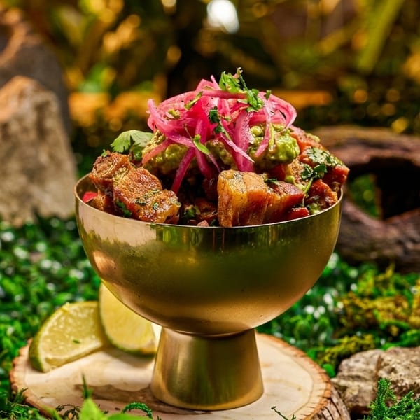 Golden bowl of pork belly, guacamole, and pickled onions on a mossy, jungle-like setting.